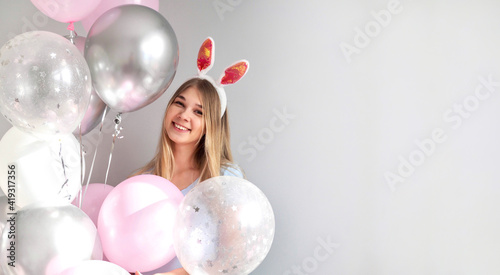 Happy girl in costume bunny with ears. Girl in rabbit costume having fun with pink balloons. Happy easter banner. Young smiling woman wearing bunny ears on Easter day. Easter Bunnies. Copy space