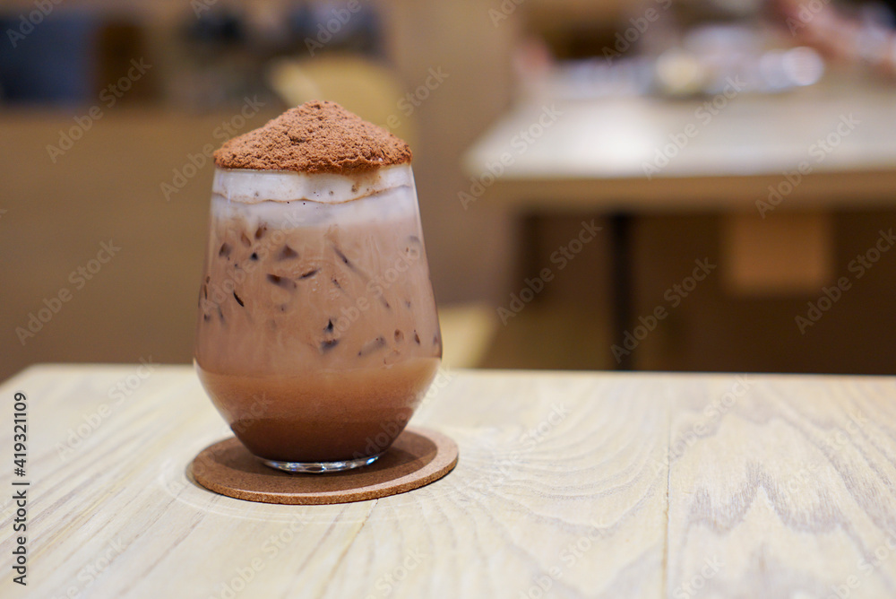 Iced Chocolate Bomb topped with cocoa powder likes volcano on wooden table in cafe. Iced Chocolate Bomb topped with cocoa powder likes volcano on wooden table in cafe.
