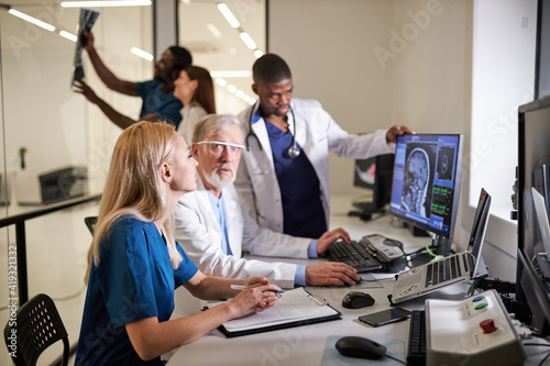 Diverse Doctors and Radiologists Discuss Diagnosis while Looking at Computer Tomography X-ray image Brain Scans Results, Discussing. Focus On Blond Nurse sitting At Desk