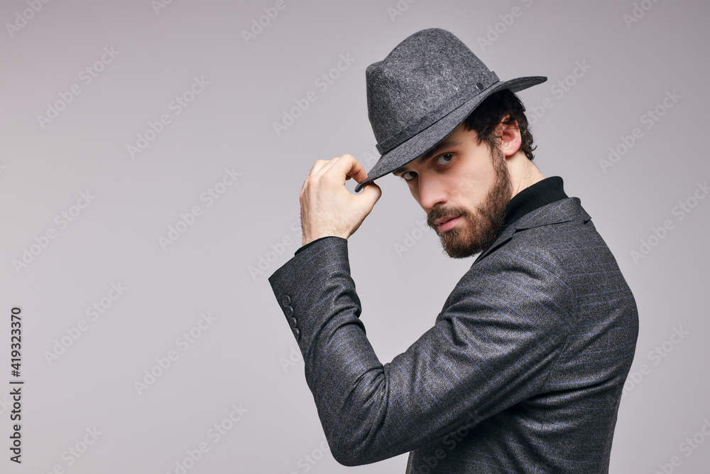 Side View Portrait of Young Male In Suit Posing Looking At Camera, Touching Hat. Young Confident Guy Alone Posing In Studio