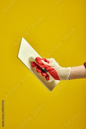 cropped hand holding a rubber grout float isolated on yellow background used for scraping the excess grout from the tile faces. copy space