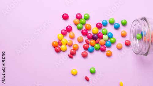 colorful candies poured from a glass jar on a colored background