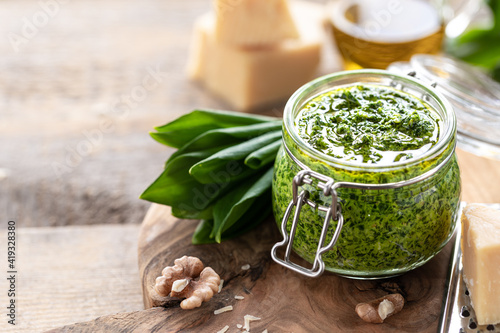 Wild leek pesto with olive oil and parmesan cheese in a glass jar on a wooden table. Useful properties of ramson. Leaves of fresh ramson. Copy space photo