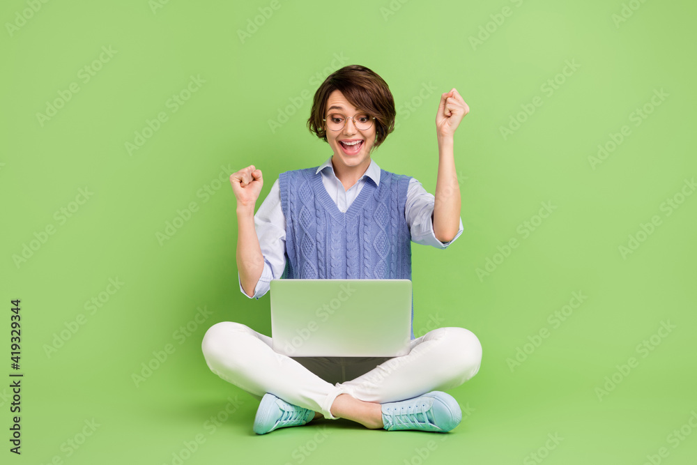 Portrait of attractive trendy lucky cheerful girl sitting lotus position using laptop rejoicing having fun isolated over green color background Portrait of attractive trendy lucky cheerful girl sitting lotus position using laptop rejoicing having fun isolated over green color background