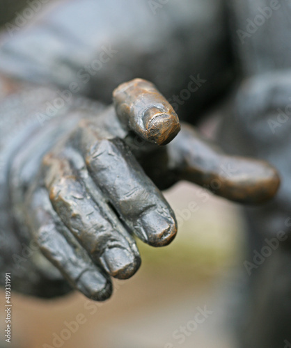 the bronze statue's hand points its index finger at a camera with a blurred background