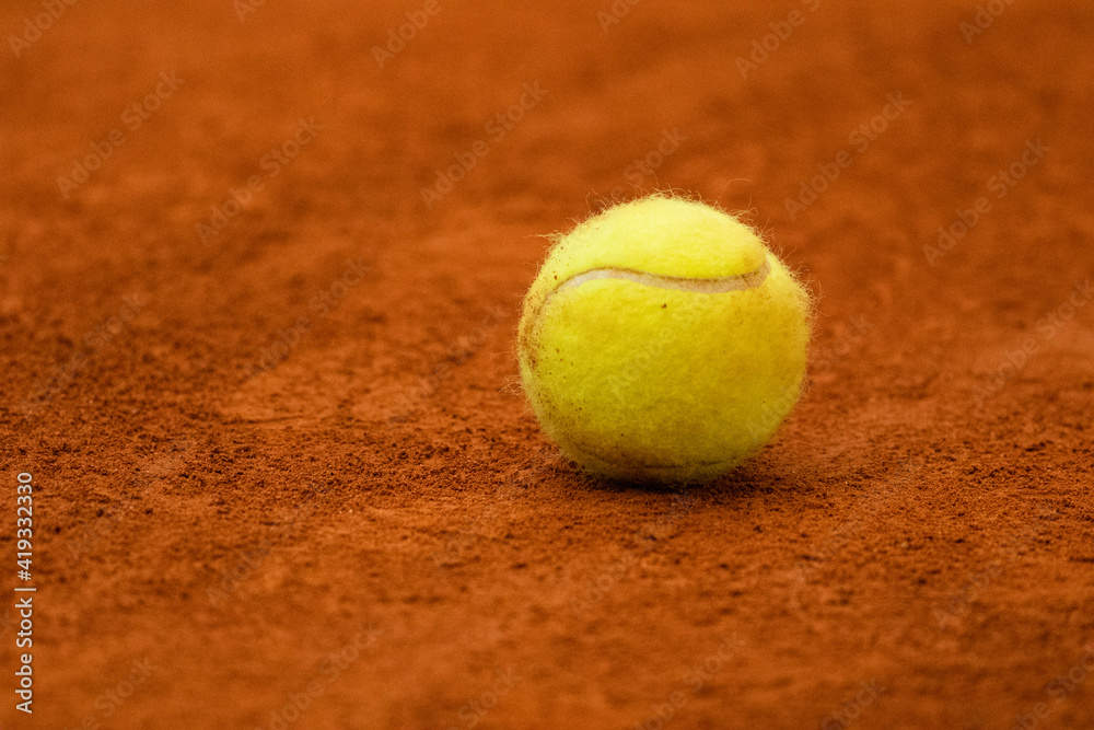 Tennis ball in classic fluorescent yellow lies on the surface of a tennis court