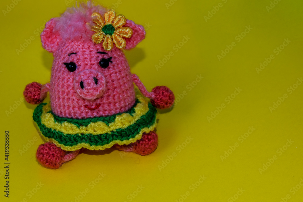 Pink, crocheted pig in a green skirt on a yellow background. Knitted toy pig.