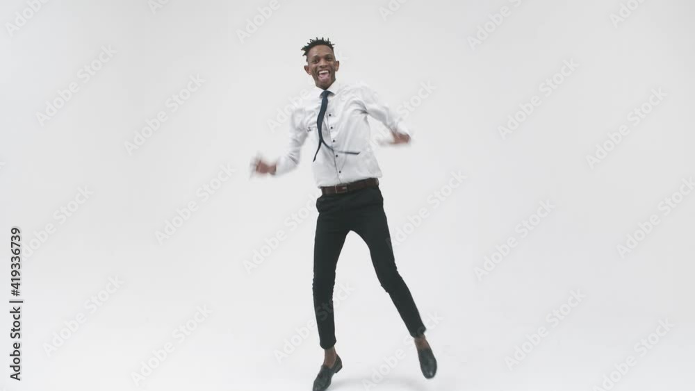 A black man smiles and dances side jumping in the studio. Black happy man in an office suit is dancing for joy on a white background. A black man smiles and dances side jumping in the studio. Black happy man in an office suit is dancing for joy on a white background.