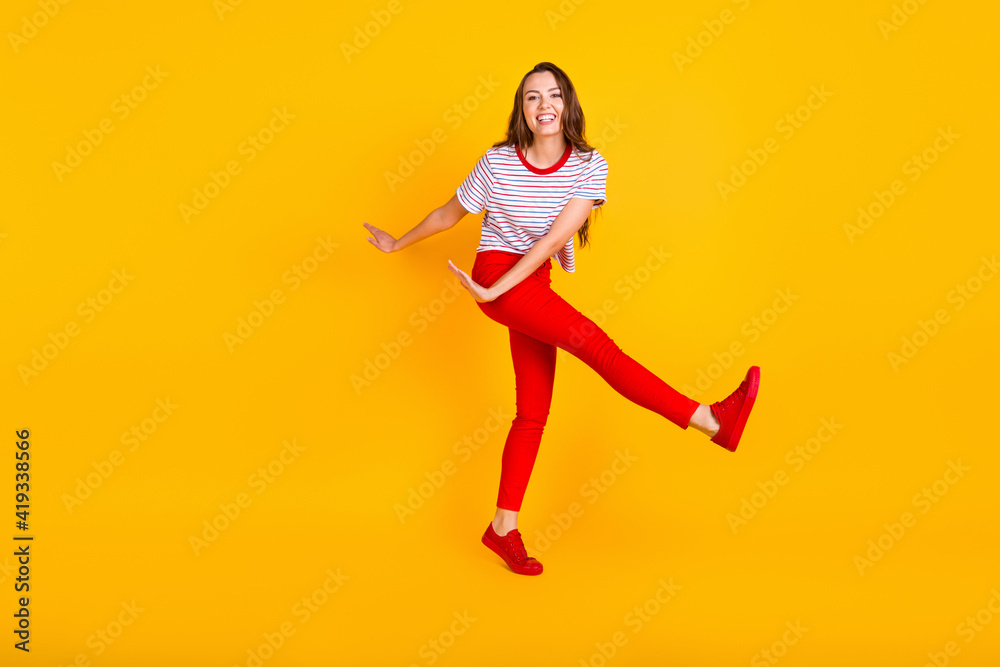 Photo of carefree lady dance have fun wear striped shirt red trousers sneakers isolated yellow color background
