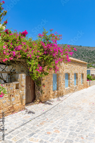Traditional alley of Mani region with a narrow street, stone built houses and a blooming bougainvillea in Limeni village, South Peloponnese , Greece.