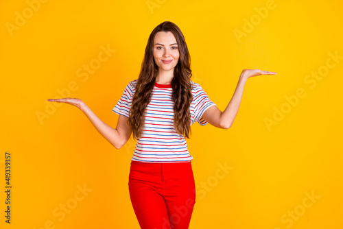 Portrait of attractive confident cheerful girl holding on two palms copy empty space ad offer isolated over vibrant yellow color background