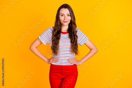 Portrait of attractive cheerful content feminine shy girl hands on hips isolated over vibrant yellow color background