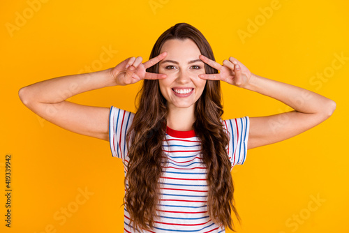 Portrait of attractive cheerful glad girl showing double v-sign near eye good mood having fun isolated over bright yellow color background