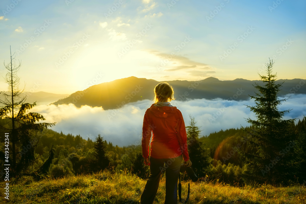 Girl tourist with a camera at dawn in the mountains. beautiful sunrise in the mountains with fog and shining sun over the mountain tops.