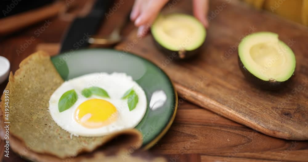 Woman preparing healthy breakfast at home, close-up on kitchen table with fried egg, pancakes and avocado Woman preparing healthy breakfast at home, close-up on kitchen table with fried egg, pancakes and avocado
