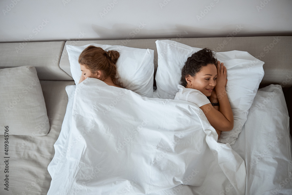 Fototapeta premium Two delighted women lying together under soft blanket