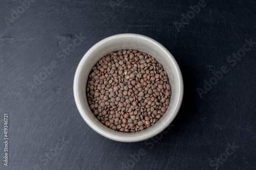 top view of a white ceramic bowl filled with fresh lentils on the center of a dark slate surface