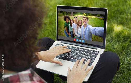 Unrecognizable young guy having video call with group of friends on laptop at park