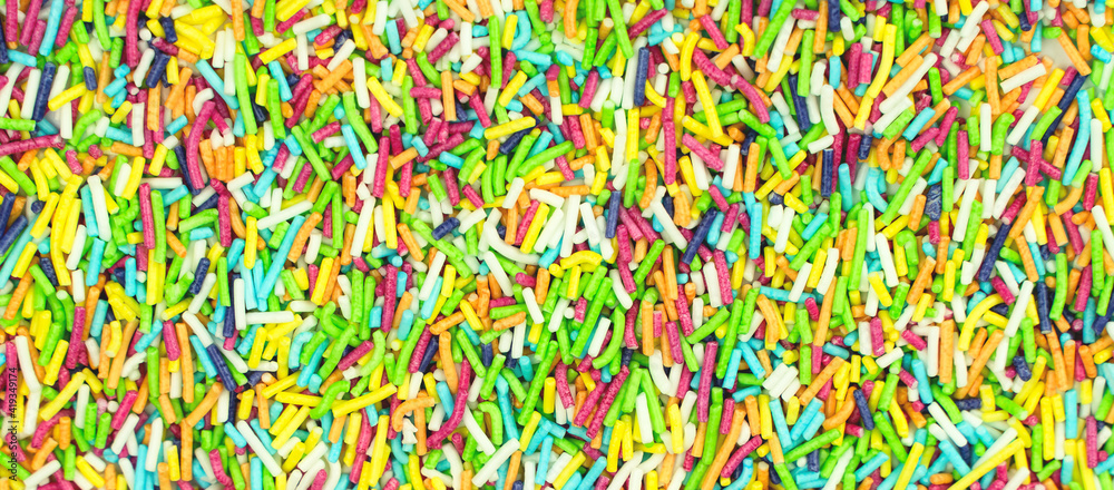 Macro of easter sprinkle. Multicolored bright rainbow background. Fun colorful sweet texture. Banner