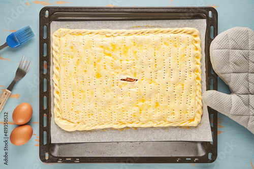Raw empanada stuffed with tuna, tomato, onion and pepper and painted with egg is on a baking tray ready to be baked. Tuna pie. Typical Galician dish from Galicia and Spain