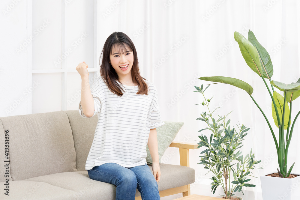 部屋のソファでガッツポーズをする若い女性 部屋のソファでガッツポーズをする若い女性