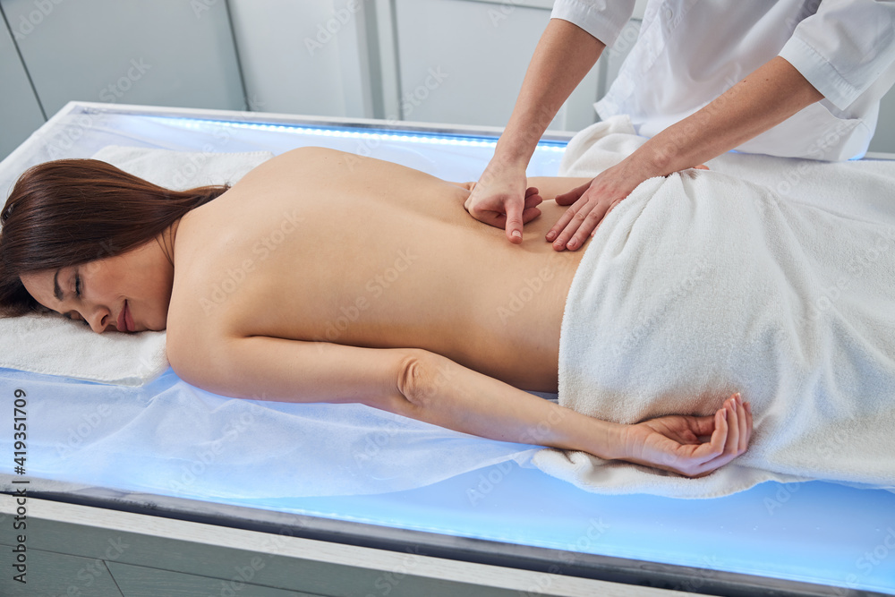 Massage expert doing knuckle work movements on naked woman back Massage expert doing knuckle work movements on naked woman back