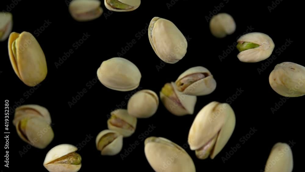 Close-up of salted pistachios flying up on a black background in slow motion Close-up of salted pistachios flying up on a black background in slow motion