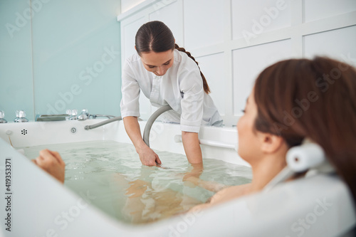 Female spa professional putting hands with hydromassage hose below water photo
