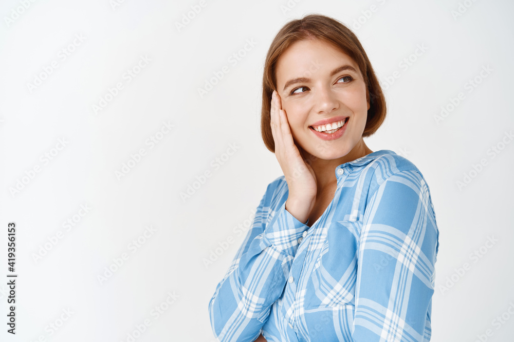 Beauty. Portrait of happy woman touching cheek and looking aside at empty space. Young girl with natural little make-up, healthy perfect skin after daily care cosmetics, white background Beauty. Portrait of happy woman touching cheek and looking aside at empty space. Young girl with natural little make-up, healthy perfect skin after daily care cosmetics, white background
