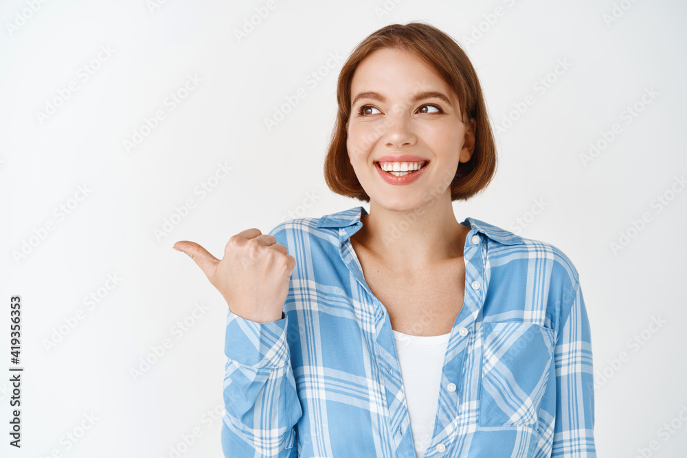 Portrait of beautiful girl with short hair and natural face light make-up, pointing left and looking at logo banner, showing empty space for advertisement, white background Portrait of beautiful girl with short hair and natural face light make-up, pointing left and looking at logo banner, showing empty space for advertisement, white background