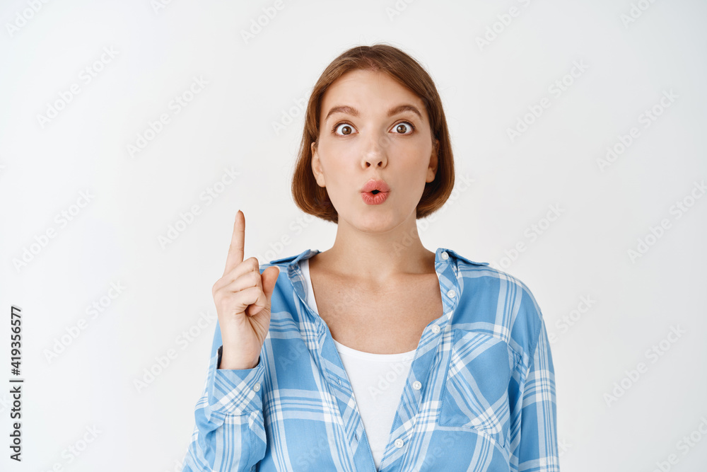 Wow look there. Excited caucasian girl looking amazed, pointing finger up and look astonished, showing interesting promo deal, standing on white background Wow look there. Excited caucasian girl looking amazed, pointing finger up and look astonished, showing interesting promo deal, standing on white background