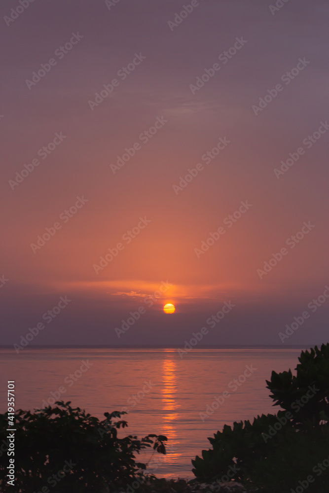 Amazing purple evening sky over Indian ocean. Idyllic sunset over tropical beach with trees silhouettes. Sunset with sunny path in evening dusk. Tranquil twilight over calm water. Peaceful seascape.