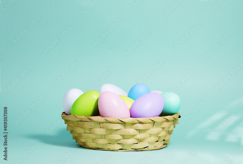 Easter background. A collection of Easter eggs in pastel colors in a basket on a blue-green background, with harsh shadows and light. Easter background. A collection of Easter eggs in pastel colors in a basket on a blue-green background, with harsh shadows and light.