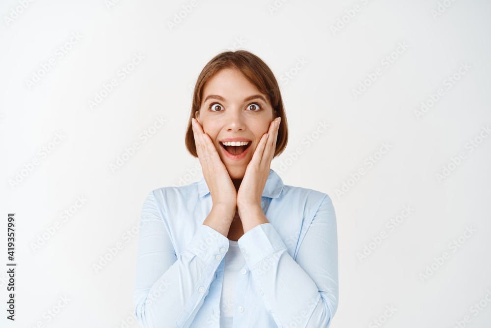Lucky excited woman looking with surprise and amazement at camera, winning and feeling joy, touching cheeks and smiling astonished, white background