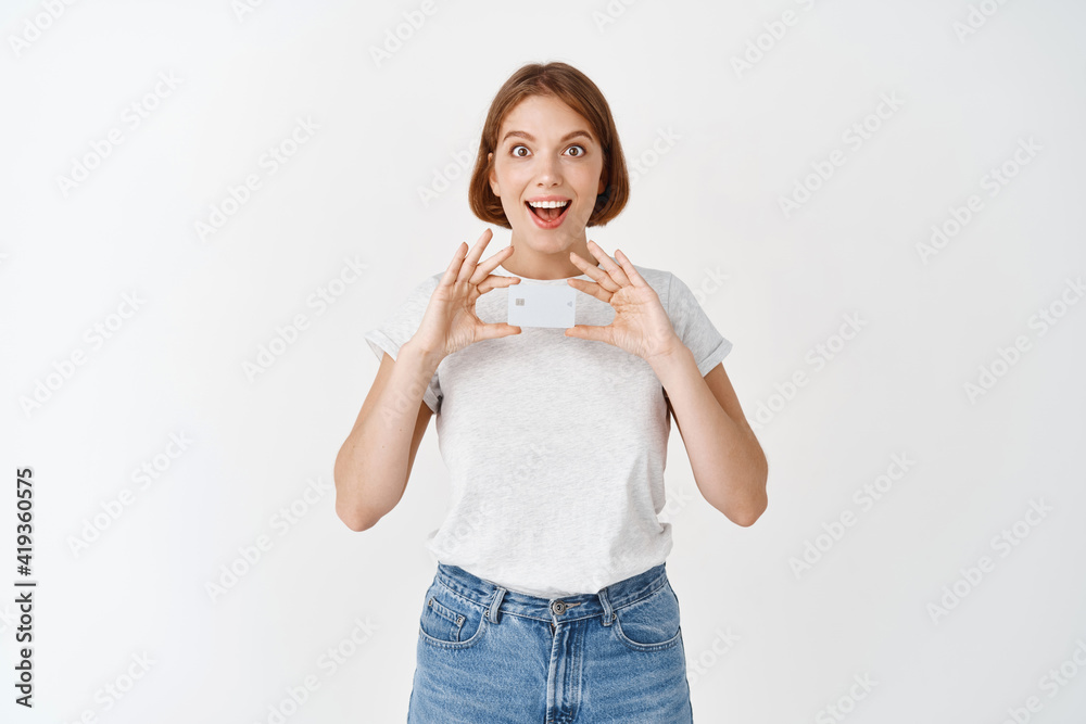 Portrait of excited girl showing plastic credit card, recommend bank offer, standing against white background Portrait of excited girl showing plastic credit card, recommend bank offer, standing against white background