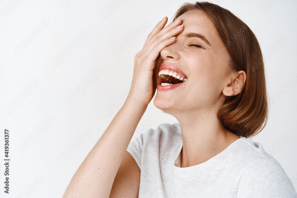 Close up portrait of happy beautiful woman with short haircut, laughing and touching face, looking aside. Candid girl showing positive emotions, white background Close up portrait of happy beautiful woman with short haircut, laughing and touching face, looking aside. Candid girl showing positive emotions, white background