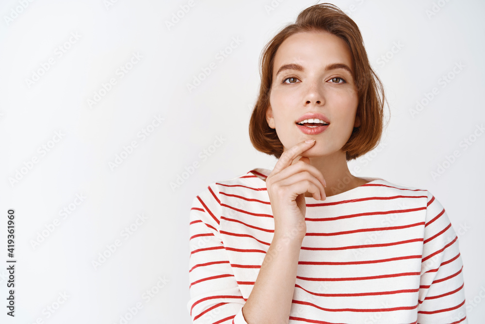 Beautiful woman looking thoughtful and sensual at camera, touching lip with opened mouth, pondering something interesting, standing against white background Beautiful woman looking thoughtful and sensual at camera, touching lip with opened mouth, pondering something interesting, standing against white background