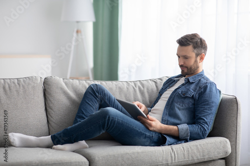 Happy man laying on couch at home, using digital tablet