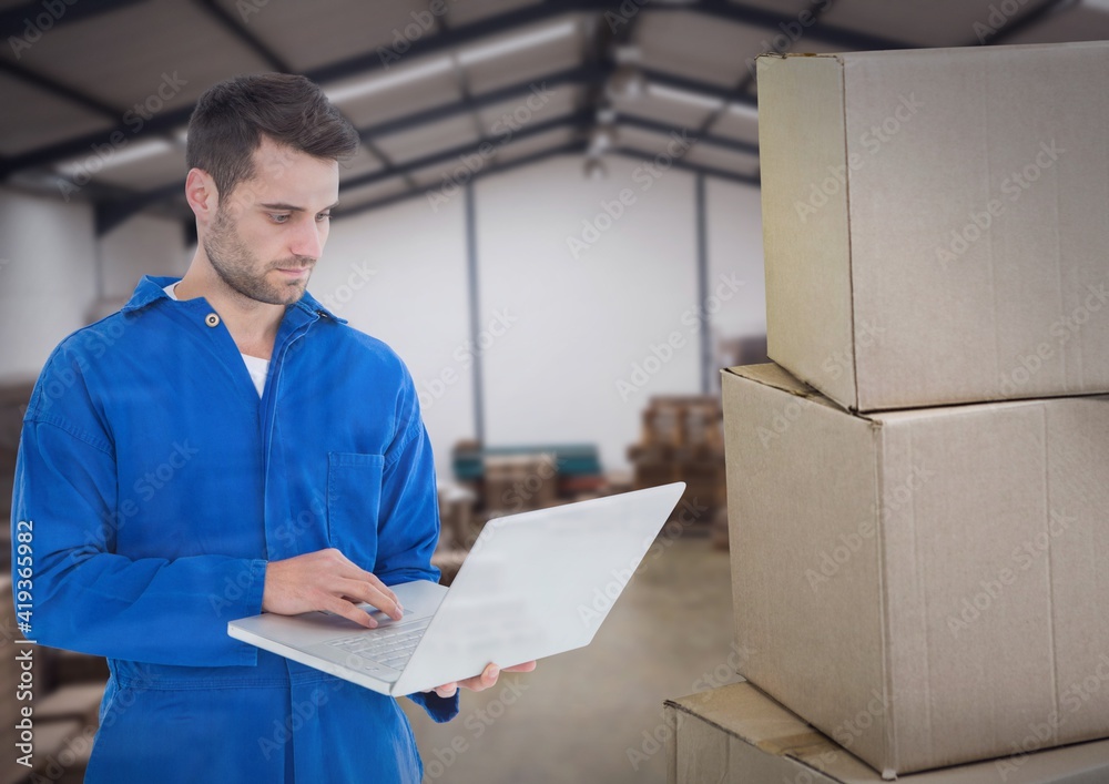 Composition of warehouse worker using laptop over stack of cardboard boxes in warehouse Composition of warehouse worker using laptop over stack of cardboard boxes in warehouse