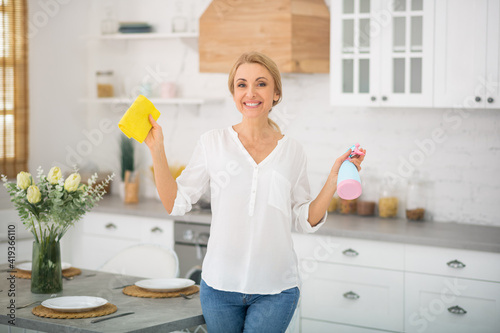 Blonde woman in jeans and shirt holding a disinfecting spray in hands