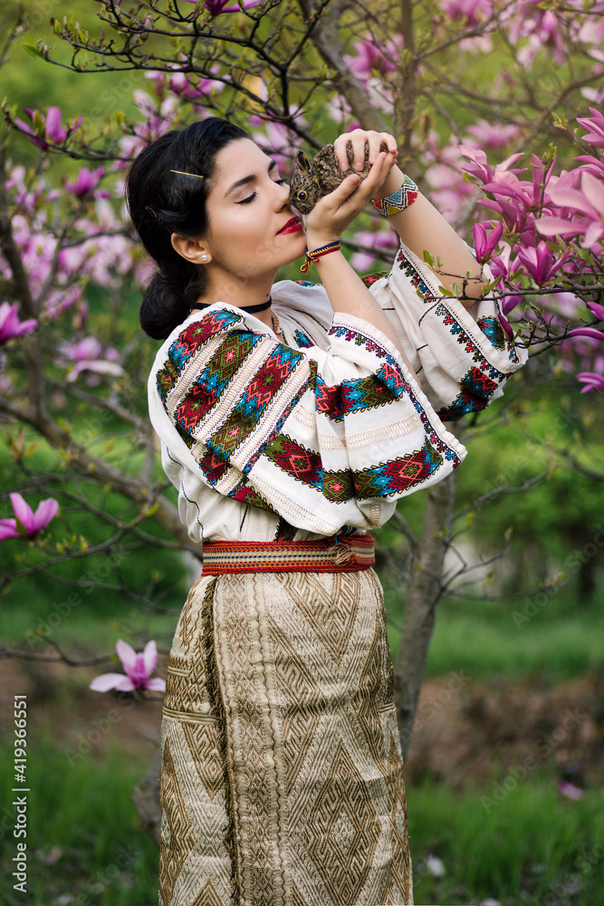 Beautiful young woman posing in romanian traditional costume with a little rabbit in a magnolia orchard Beautiful young woman posing in romanian traditional costume with a little rabbit in a magnolia orchard
