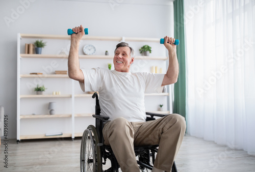 Physical activities for disabled elderly adults. Handicapped man in wheelchair making exerises with dumbbells at home