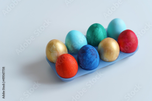 Colorful Easter eggs in blue plastic egg stand on white table. Easter concept, copy space. Minimalist style