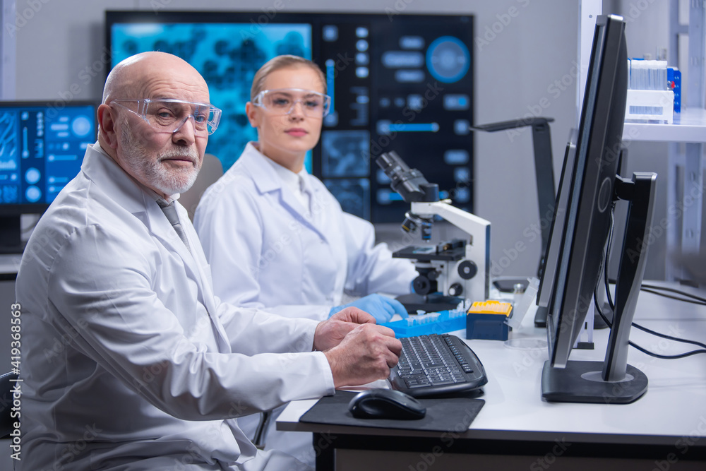 Professor and his young and professional laboratory assistant are doing scientific experiment in a modern laboratory. Genetic engineers workplace. The concept of science, medicine and vaccine. Professor and his young and professional laboratory assistant are doing scientific experiment in a modern laboratory. Genetic engineers workplace. The concept of science, medicine and vaccine.