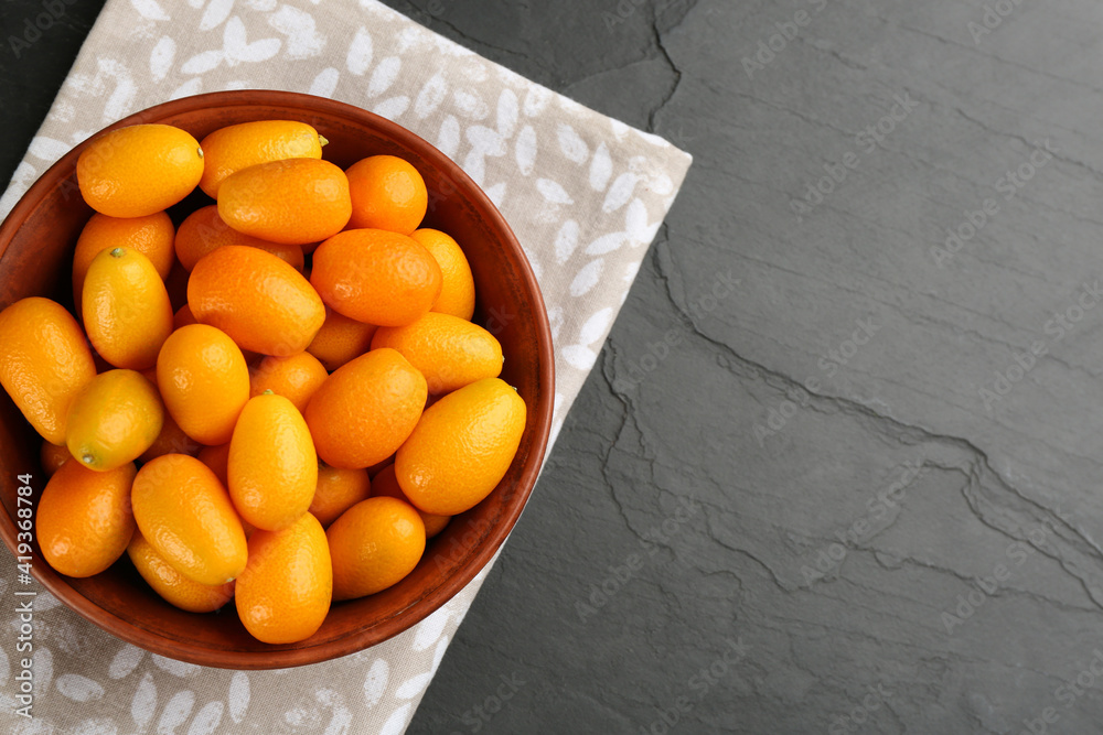 Fresh ripe kumquats in bowl on black table, top view. Space for text Fresh ripe kumquats in bowl on black table, top view. Space for text