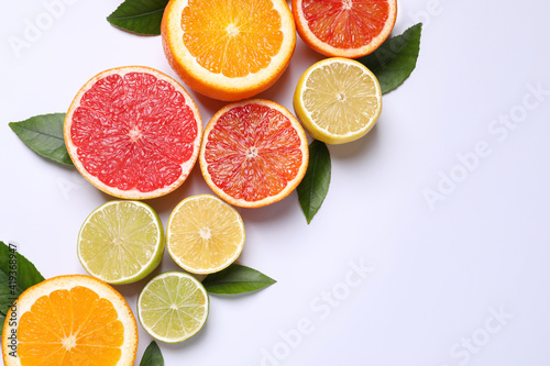 Fresh juicy citrus fruits with green leaves on white background, flat lay. Space for text
