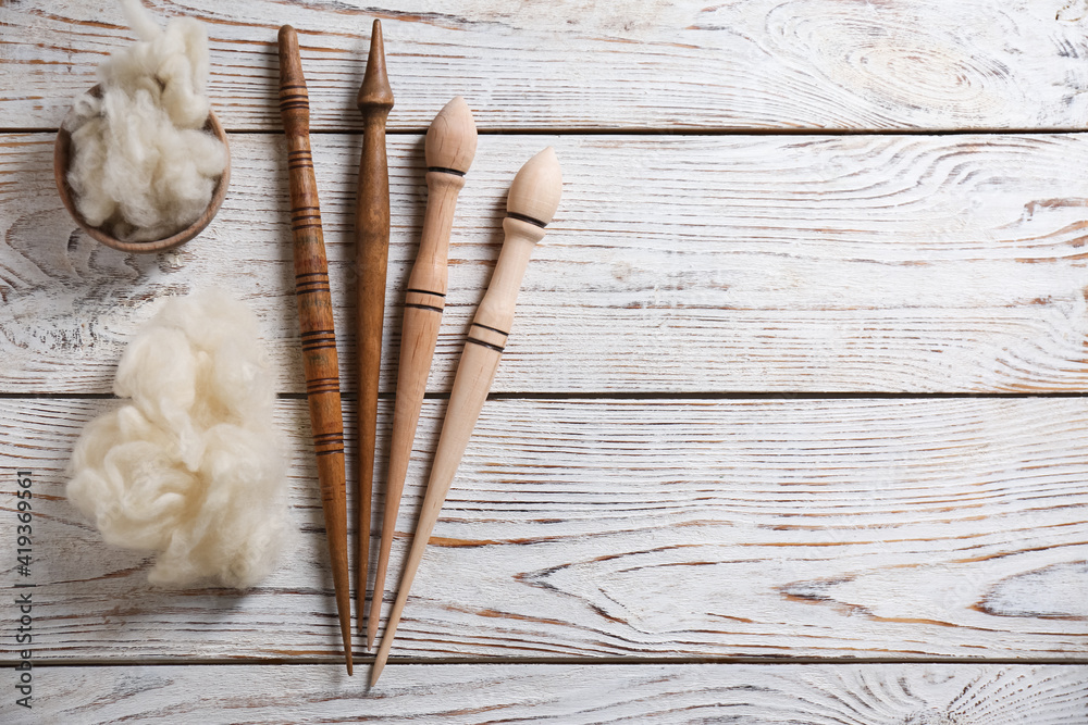 Soft wool and spindles on white wooden table, flat lay. Space for text Soft wool and spindles on white wooden table, flat lay. Space for text
