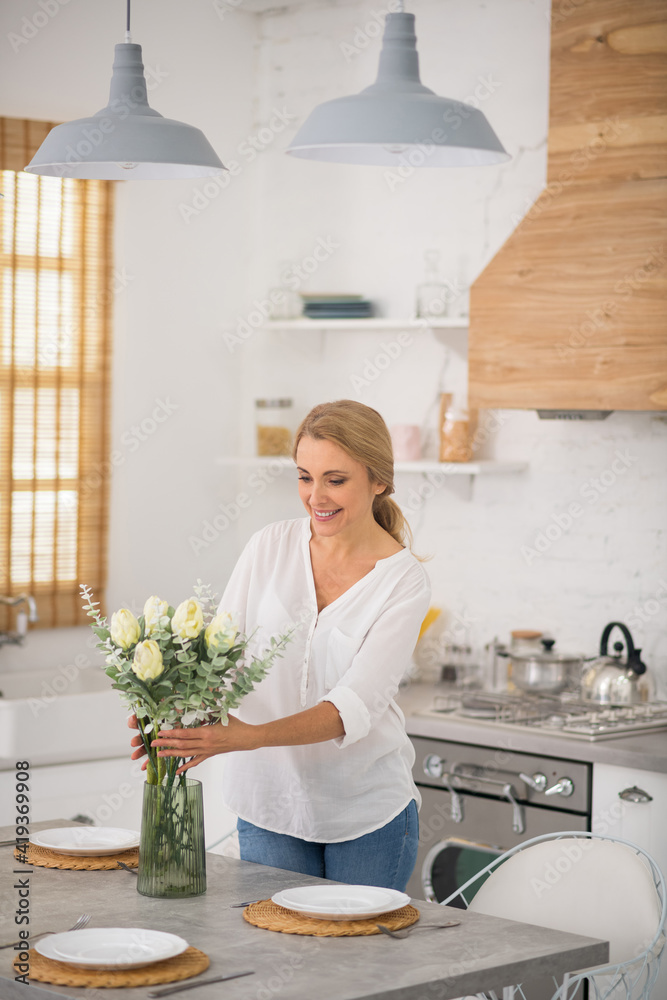 Blonde housewife in jeans putting flowers into the vase Blonde housewife in jeans putting flowers into the vase
