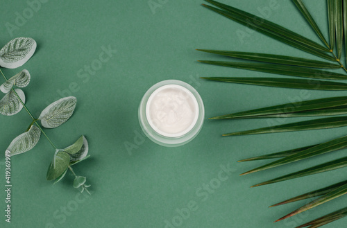 Top view of an open jar of cream and green leaves on a colored background. Beauty concept with cosmetic products for the face.