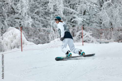 cheerful woman riding on snowboard in the mountains in winter. woman in white ski suit